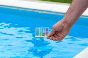 hand holding the pool testing kit above a swimming pool, testing chemical quality